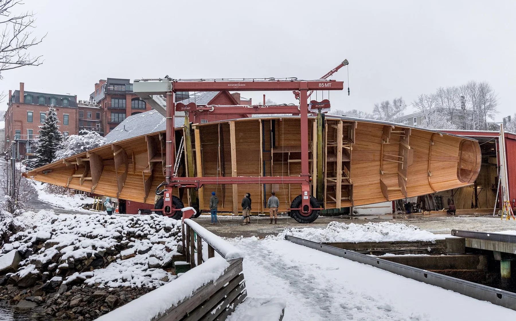 The inverted hull of the 95-foot Ouzel outdoors in snow beneath a gantry, before being turned upright.