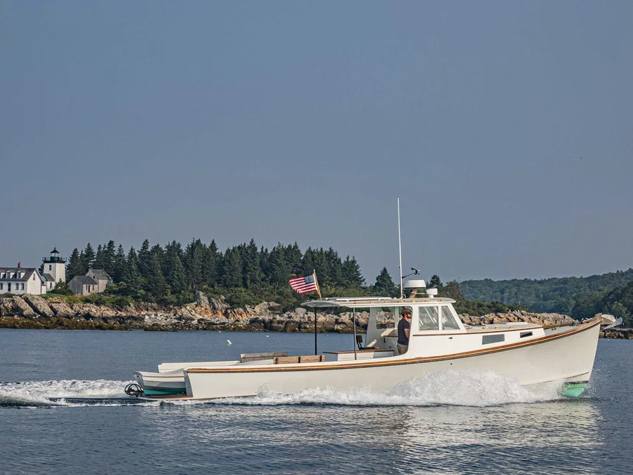 A white powerboat under way past a lighthouse at the entrance to a Maine harbour.